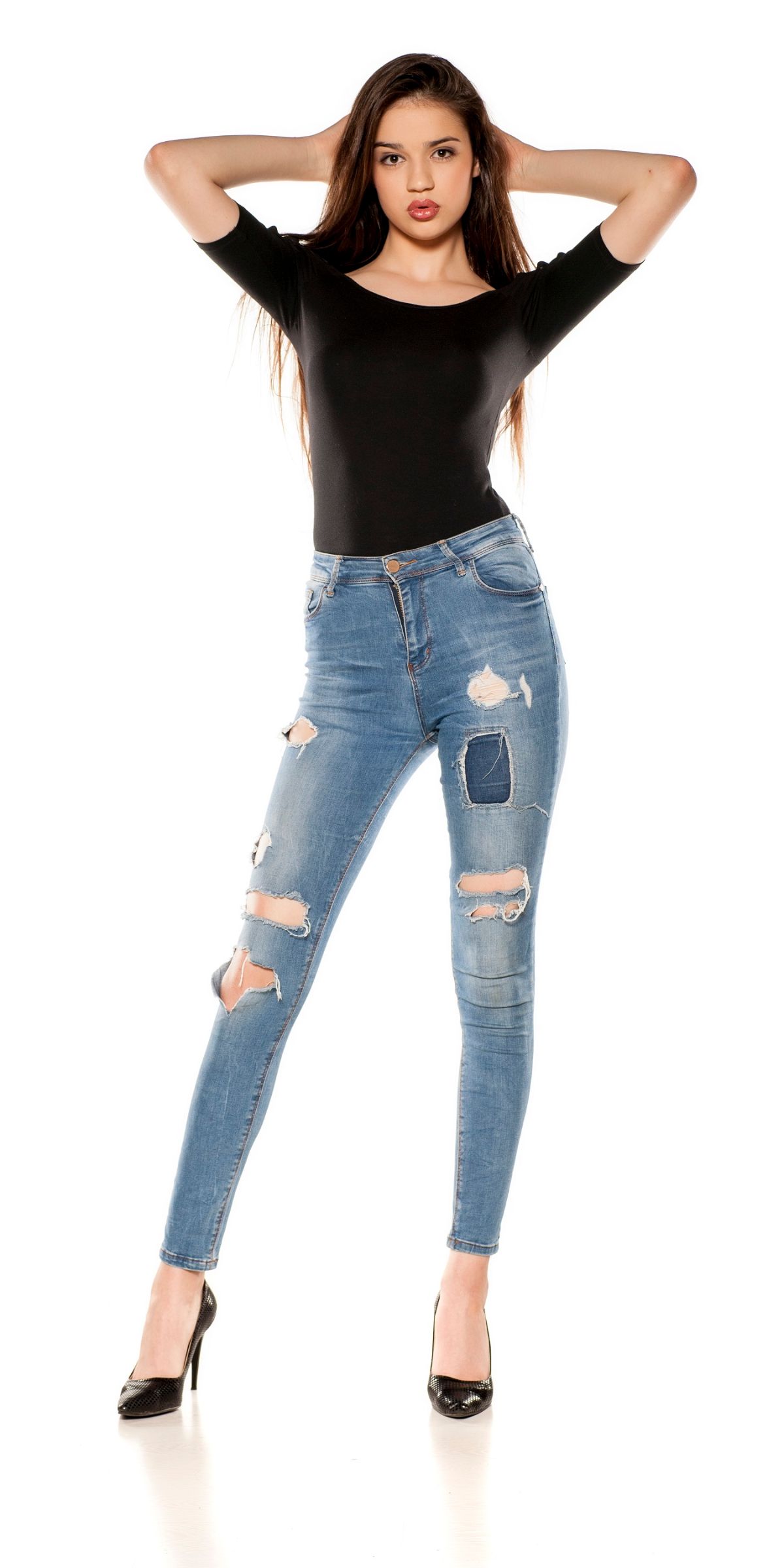 Hübsches brünettes Model mit sinnlichen Lippen und langen glatten Haaren trägt eine moderne löchrige Jeans und schwarze High Heels Pumps